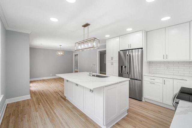 kitchen featuring stainless steel fridge, a sink, ornamental molding, a kitchen island with sink, and backsplash