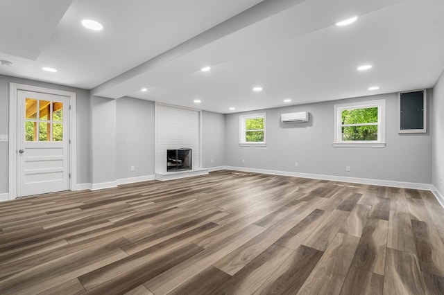 basement with an AC wall unit, wood finished floors, baseboards, a brick fireplace, and recessed lighting