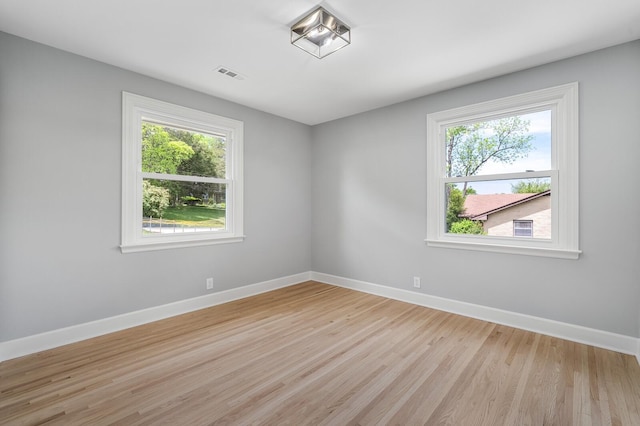 spare room featuring plenty of natural light, light wood finished floors, and baseboards