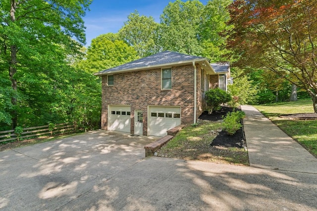 view of side of home featuring fence, an attached garage, driveway, and brick siding