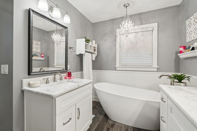 full bath featuring a chandelier, wood finished floors, a freestanding bath, vanity, and a wainscoted wall