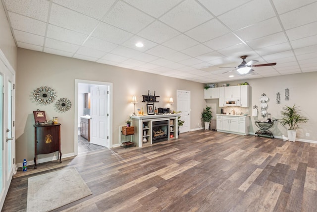 living room featuring baseboards, dark wood finished floors, a drop ceiling, a ceiling fan, and recessed lighting