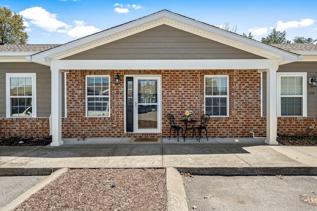 rear view of property featuring brick siding, a patio, and a shingled roof