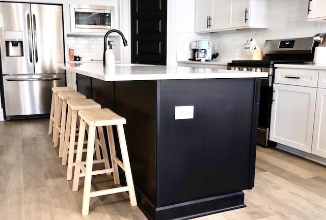 kitchen featuring stainless steel appliances, tasteful backsplash, a breakfast bar area, a center island with sink, and light countertops