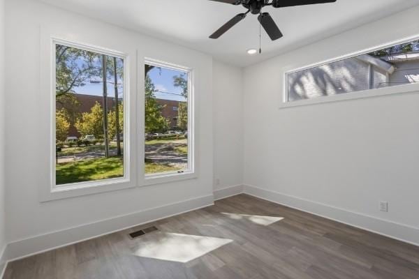 spare room featuring plenty of natural light, dark wood finished floors, baseboards, and ceiling fan