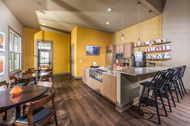 kitchen with stainless steel microwave, dark wood-style floors, a kitchen breakfast bar, backsplash, and a peninsula