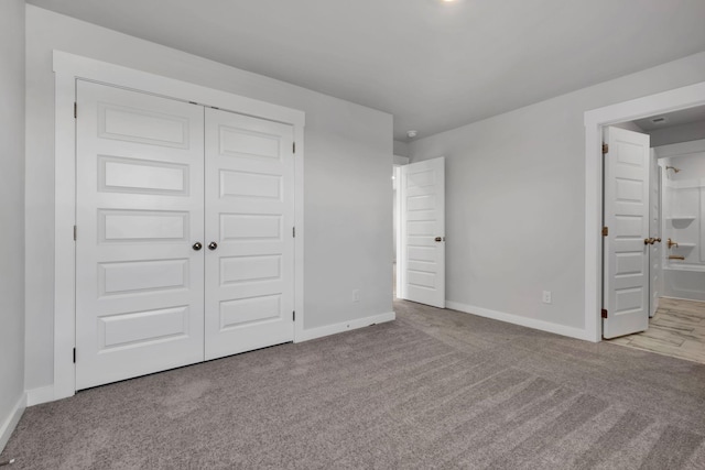 unfurnished bedroom with baseboards, carpet floors, a closet, and ensuite bathroom