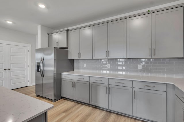 kitchen with stainless steel fridge, gray cabinetry, light wood-style flooring, backsplash, and recessed lighting