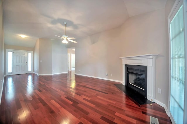 unfurnished living room with a fireplace with flush hearth, dark wood-type flooring, a ceiling fan, lofted ceiling, and baseboards