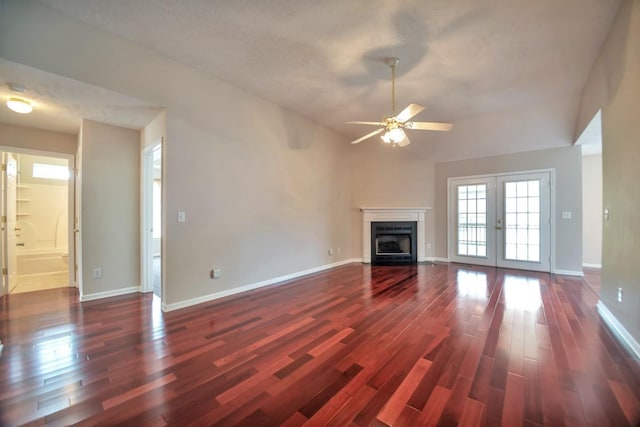 unfurnished living room with dark wood finished floors, ceiling fan, french doors, a fireplace, and vaulted ceiling