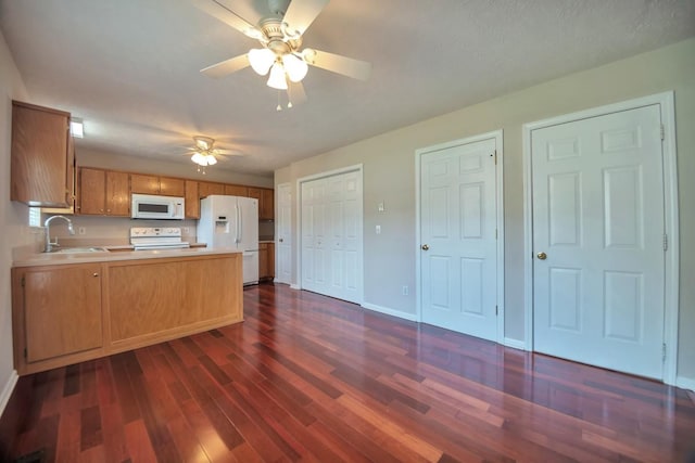 kitchen with white appliances, a peninsula, a sink, light countertops, and dark wood-type flooring