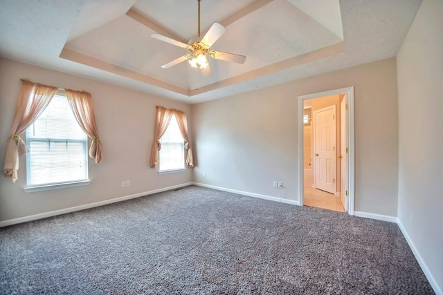 carpeted empty room featuring a raised ceiling, baseboards, and ceiling fan