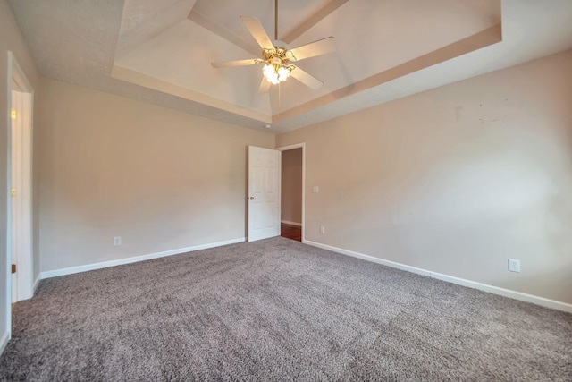carpeted empty room featuring a tray ceiling, ceiling fan, and baseboards