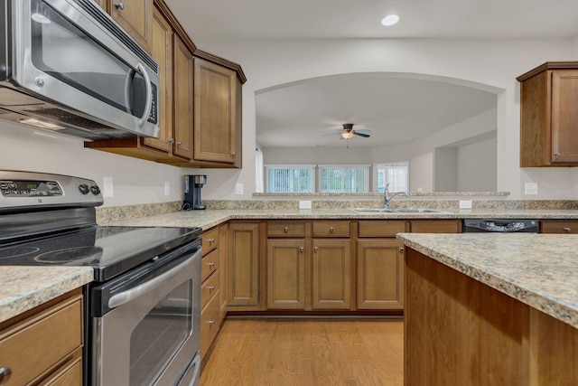 kitchen featuring stainless steel appliances, a sink, arched walkways, a ceiling fan, and light wood-style flooring