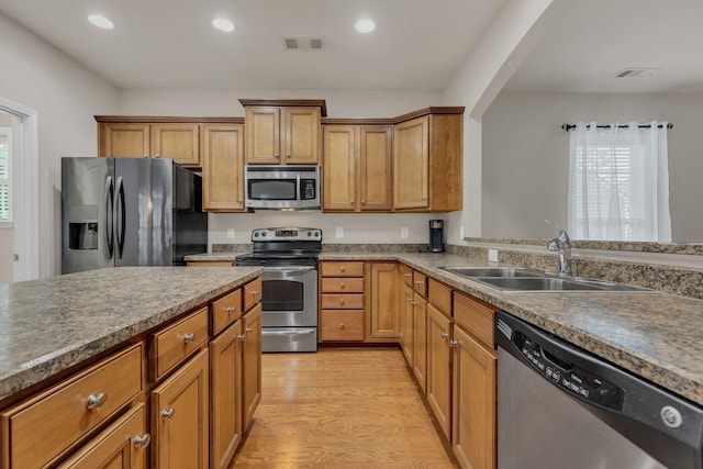 kitchen featuring appliances with stainless steel finishes, a sink, light wood-style floors, brown cabinetry, and recessed lighting