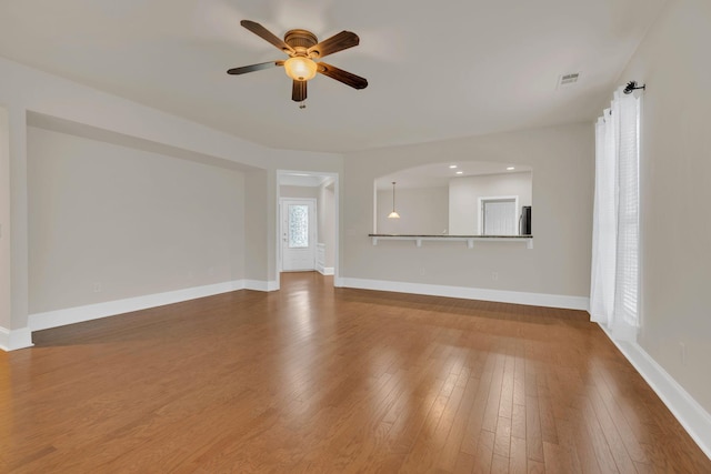unfurnished living room featuring ceiling fan, wood finished floors, baseboards, and arched walkways