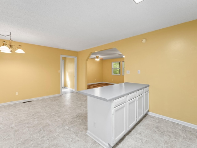 kitchen featuring arched walkways, open floor plan, white cabinets, a peninsula, and baseboards