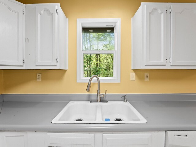 kitchen with a sink, white cabinets, white dishwasher, and light countertops