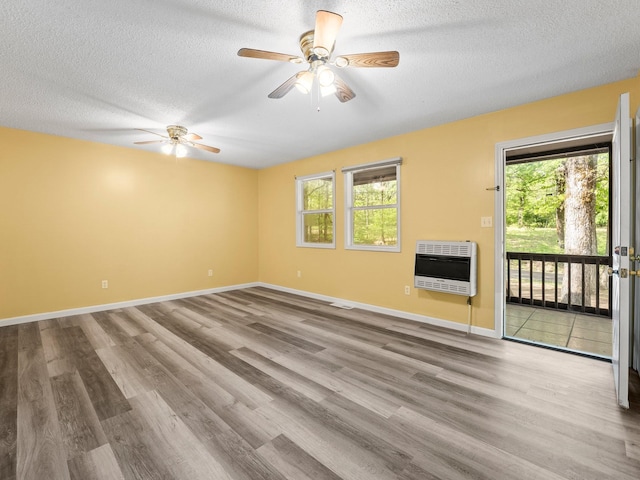 unfurnished room with heating unit, wood finished floors, healthy amount of natural light, a ceiling fan, and a textured ceiling