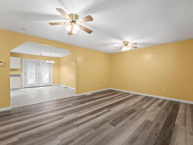 spare room featuring ceiling fan, wood finished floors, arched walkways, a textured ceiling, and baseboards