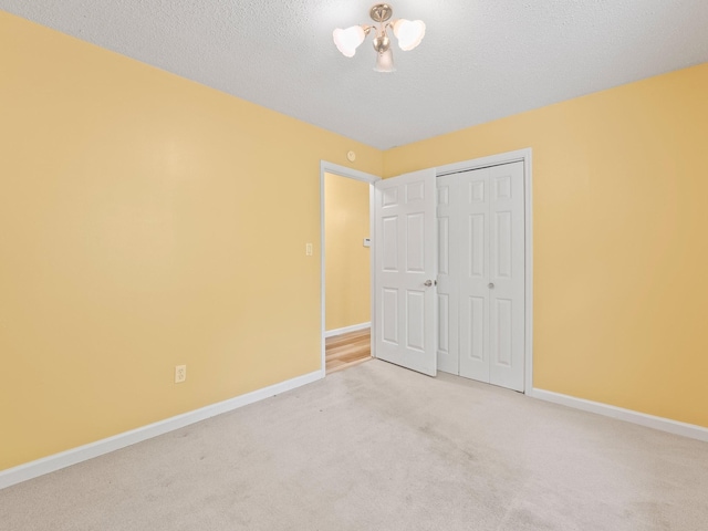 unfurnished bedroom featuring light colored carpet, baseboards, a closet, and a textured ceiling