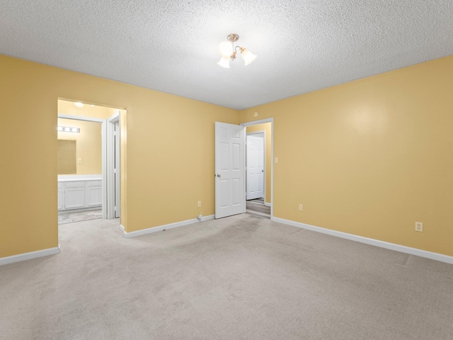 spare room featuring light carpet, baseboards, and a textured ceiling