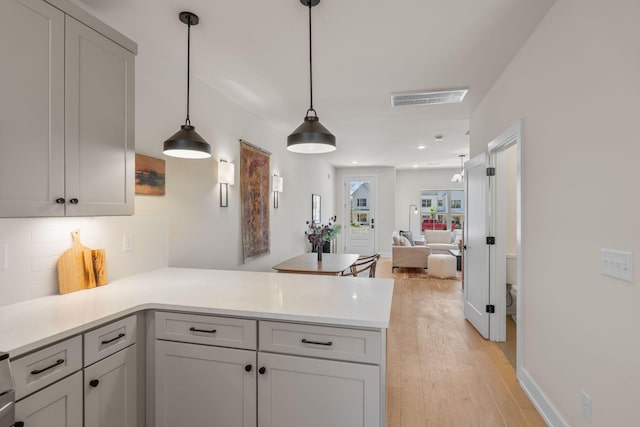 kitchen featuring a peninsula, tasteful backsplash, light wood-style flooring, light countertops, and pendant lighting