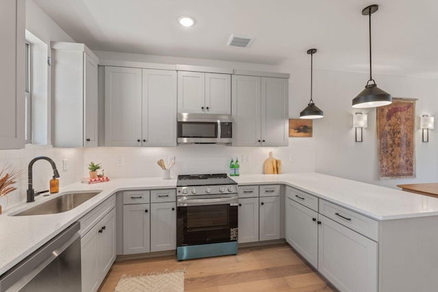 kitchen featuring stainless steel appliances, a sink, a peninsula, light countertops, and backsplash