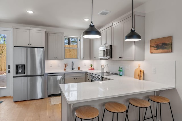 kitchen with appliances with stainless steel finishes, a sink, a peninsula, decorative backsplash, and recessed lighting