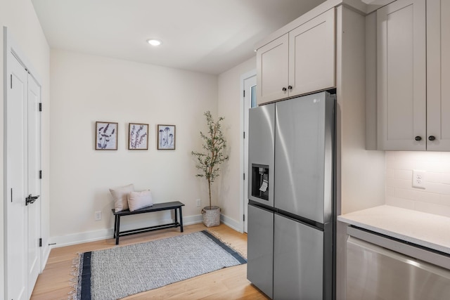 kitchen with appliances with stainless steel finishes, light wood finished floors, backsplash, light countertops, and baseboards
