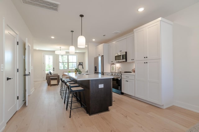 kitchen featuring appliances with stainless steel finishes, light wood-style floors, a kitchen breakfast bar, a center island with sink, and white cabinets