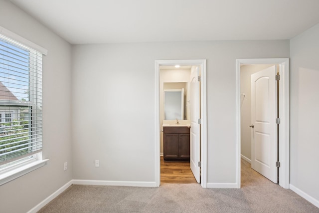 unfurnished bedroom with light colored carpet, baseboards, a sink, and ensuite bath