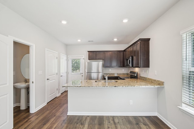 kitchen with stainless steel appliances, a sink, dark brown cabinetry, a peninsula, and light stone countertops