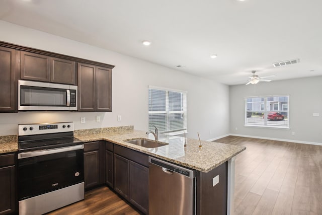 kitchen with appliances with stainless steel finishes, a sink, dark brown cabinets, a peninsula, and open floor plan