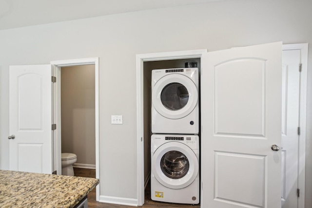 laundry area featuring stacked washer / dryer, dark wood-type flooring, and baseboards