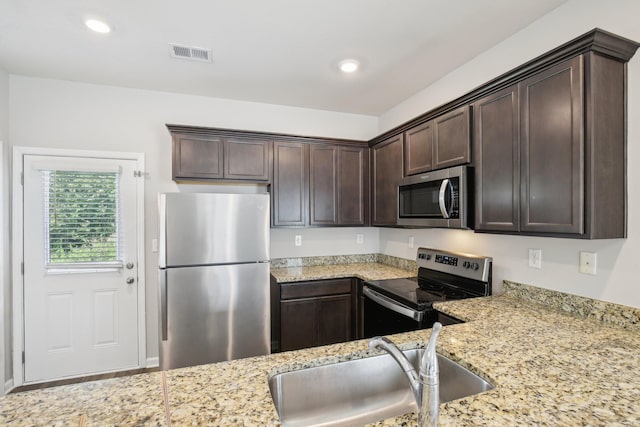 kitchen with appliances with stainless steel finishes, a sink, dark brown cabinets, light stone counters, and recessed lighting