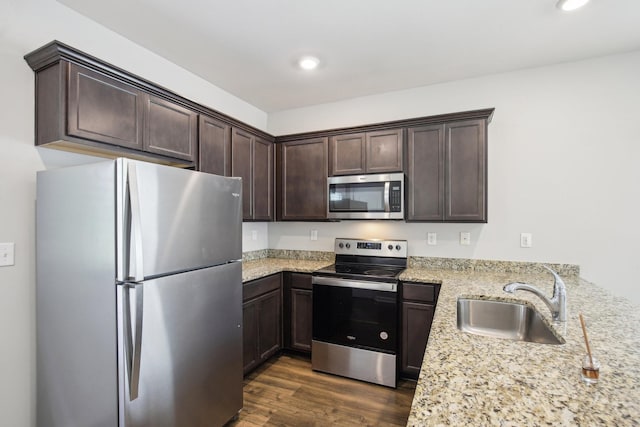 kitchen featuring stainless steel appliances, a sink, dark brown cabinetry, dark wood-style flooring, and recessed lighting