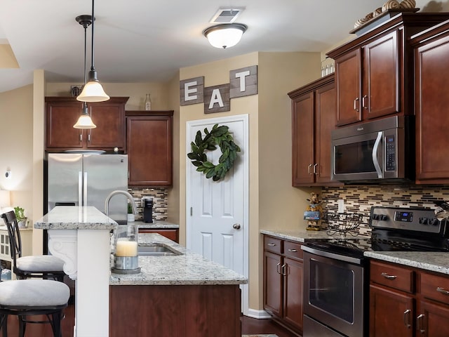 kitchen featuring appliances with stainless steel finishes, a sink, decorative backsplash, an island with sink, and pendant lighting