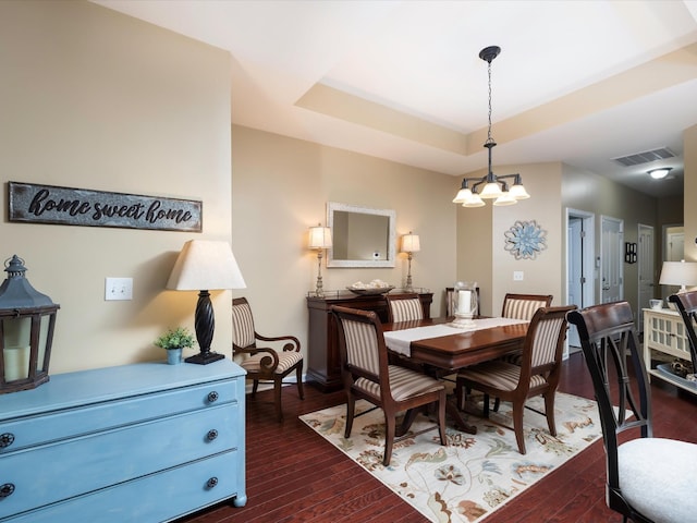 dining room with dark wood-style floors, a chandelier, a tray ceiling, and baseboards