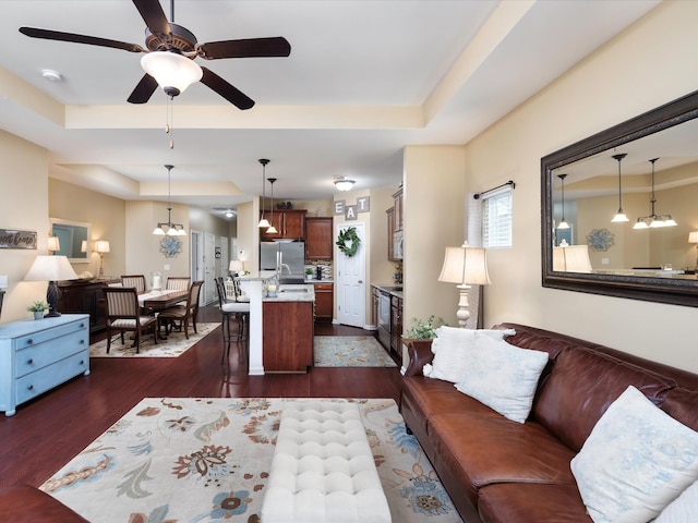 living room with a tray ceiling, dark wood finished floors, and a ceiling fan