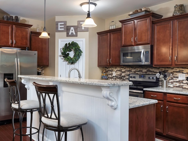 kitchen with stainless steel appliances, a kitchen breakfast bar, backsplash, light stone countertops, and hanging light fixtures