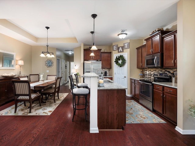 kitchen with stainless steel appliances, a sink, backsplash, a kitchen bar, and dark wood-style flooring