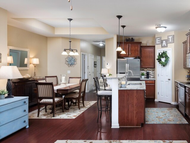 kitchen with a sink, dark wood-style floors, stainless steel appliances, a breakfast bar, and decorative light fixtures