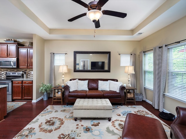 living room featuring a tray ceiling, dark wood finished floors, baseboards, and a ceiling fan