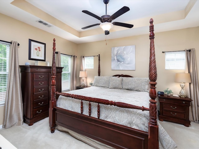 bedroom featuring light colored carpet, a tray ceiling, multiple windows, and a ceiling fan