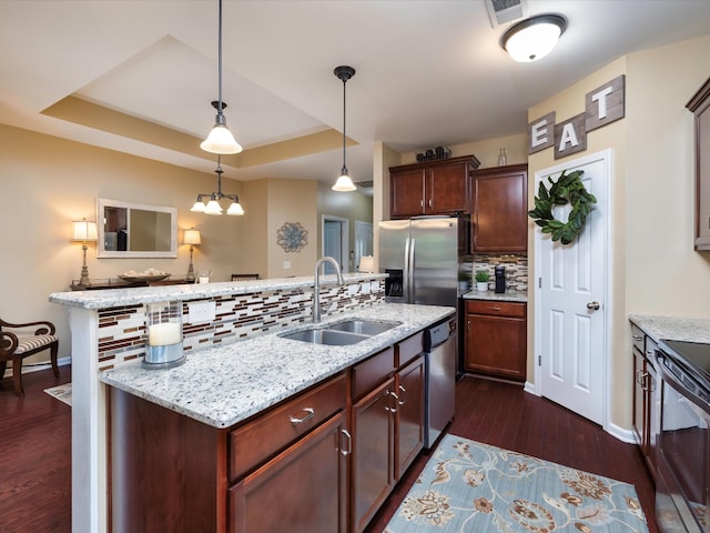 kitchen with a sink, stainless steel appliances, tasteful backsplash, dark wood-style flooring, and a center island with sink