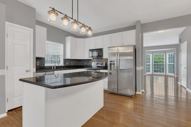 kitchen with appliances with stainless steel finishes, a sink, decorative backsplash, white cabinetry, and wood finished floors