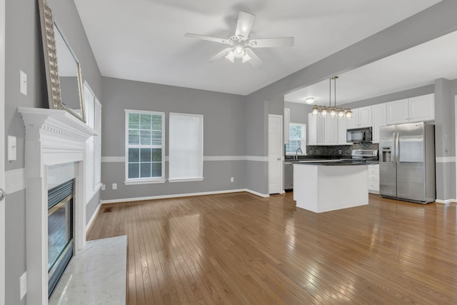 unfurnished living room with ceiling fan, wood finished floors, baseboards, and a premium fireplace