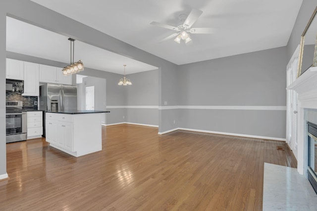 kitchen featuring stainless steel appliances, a high end fireplace, dark countertops, wood finished floors, and baseboards