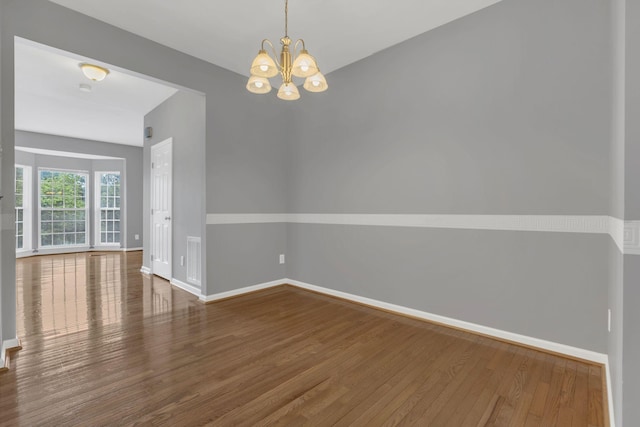 empty room with wood finished floors, baseboards, and a chandelier